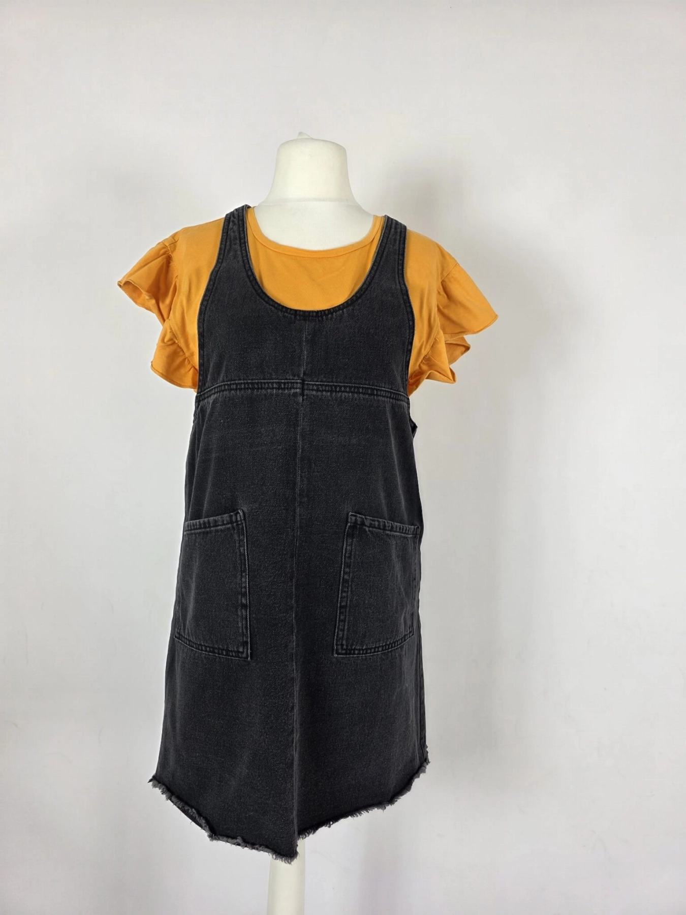 Modna stylizacja warstwowa: kremowy ażurowy sweter Vero Moda, pomarańczowy t-shirt z falbankami Costes oraz czarna sukienka jeansowa Only