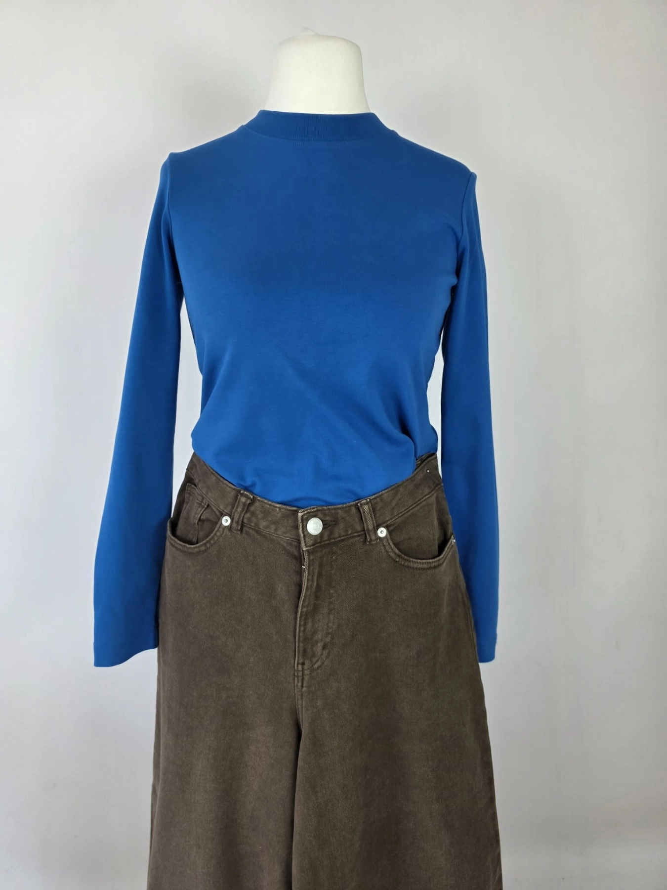 Stylowy zestaw kobiecy z niebieską bluzką COS, lnianą narzutką Zara, brązowymi spodniami wide leg Monki oraz paskiem