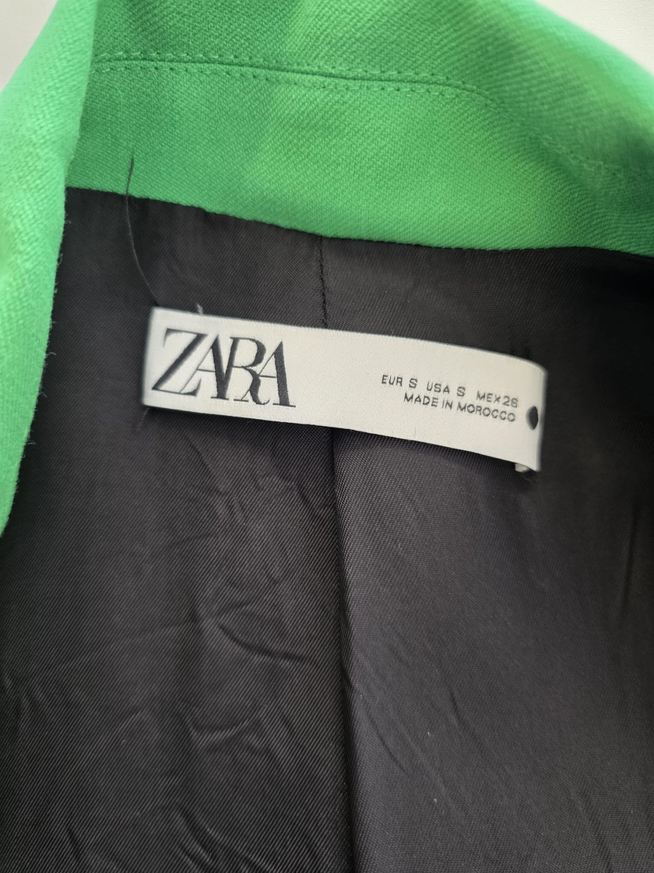 Stylowy zestaw kobiecy składający się z zielonej marynarki Zara, wzorzystej koszuli Andżela oraz czarnych jeansów Karve z wysokim stanem