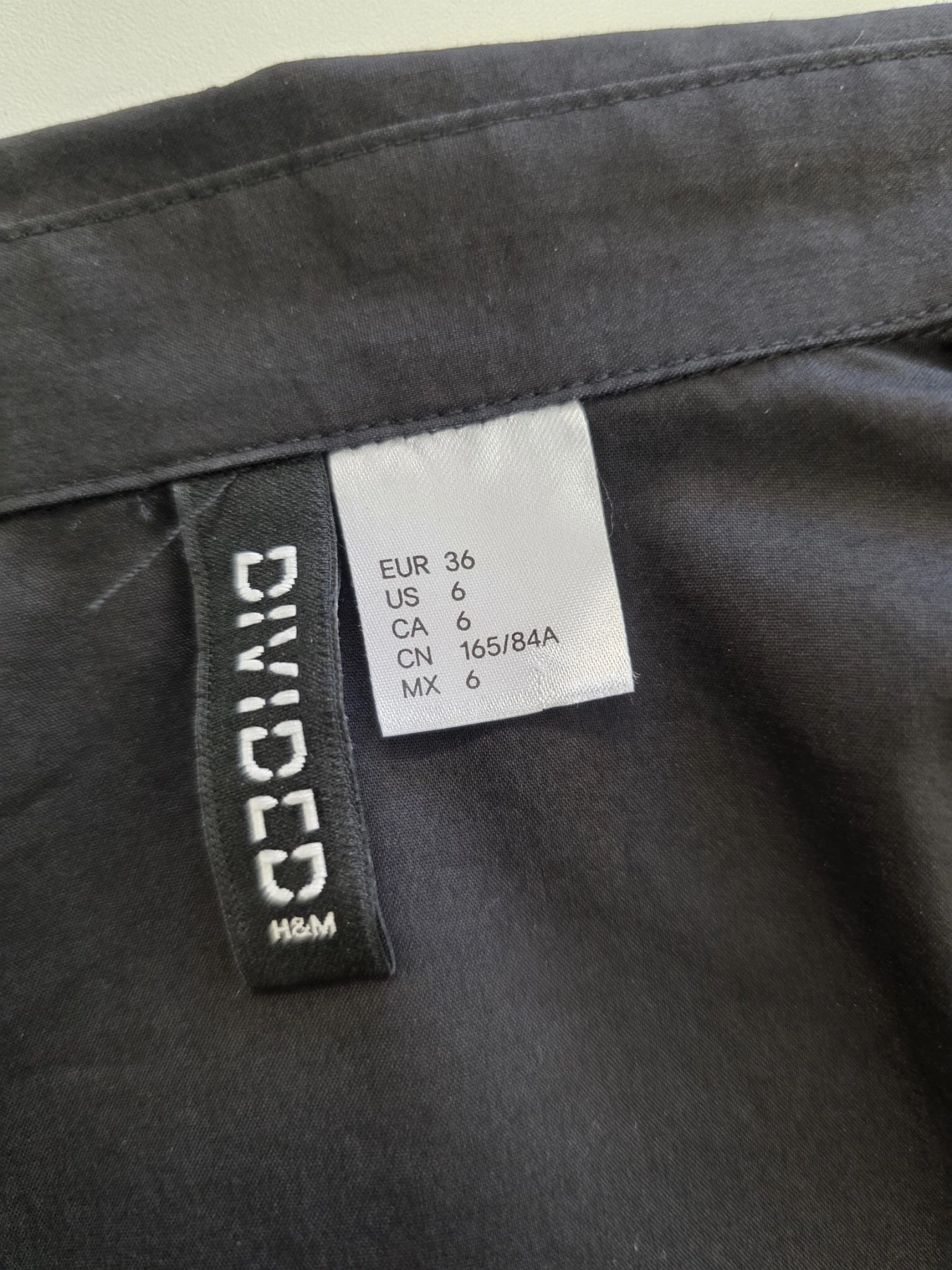 Stylizacja z czarną koszulą z falbaną Divided  i bawełnianą spódnicą mini w pepitkę od ARKET to elegancki zestaw damski podkreślający sylwetkę