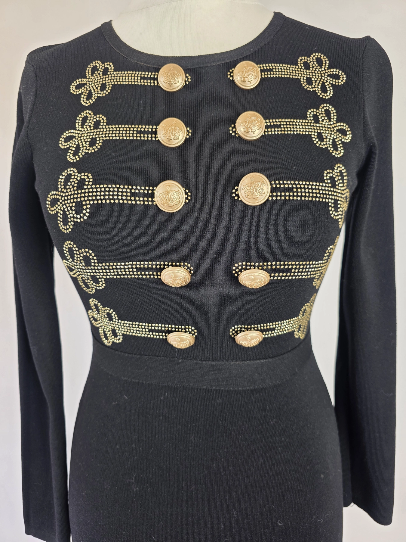 Elegancka czarna sukienka dresowa Allyson Collection ze złotymi guzikami i dżetami doskonale podkreśla kobiecą sylwetkę, łącząc styl militarny z wyjątkową wygodą