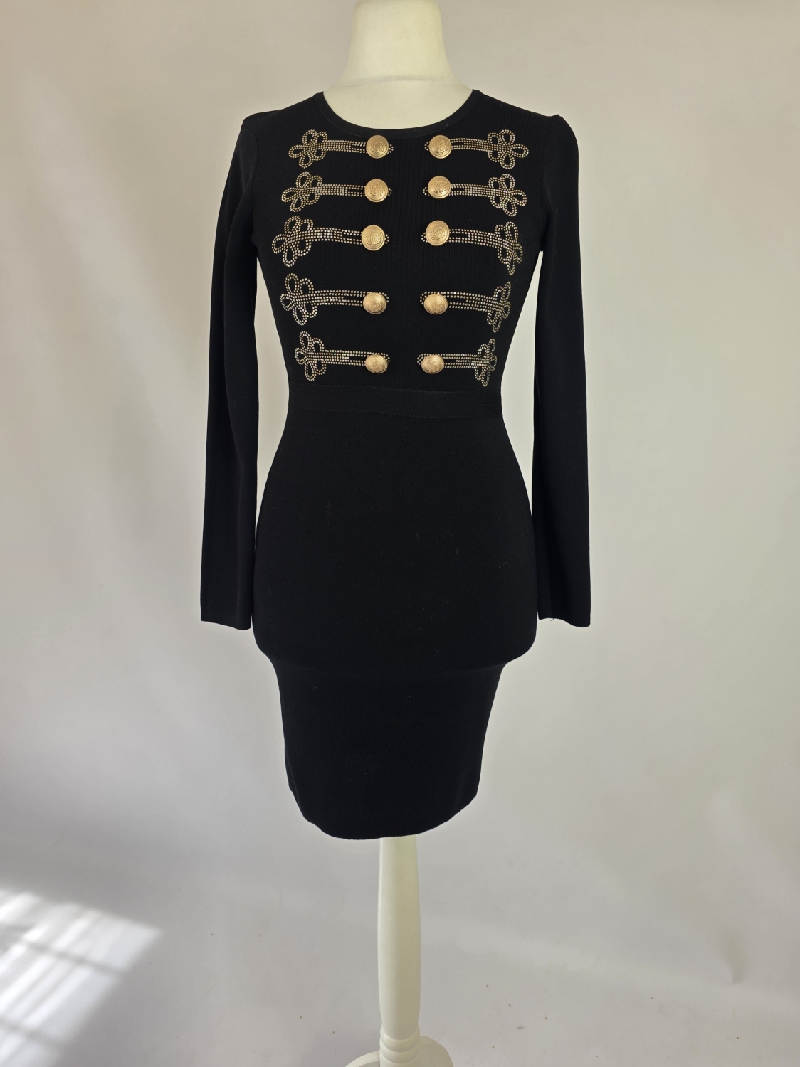 Elegancka czarna sukienka dresowa Allyson Collection ze złotymi guzikami i dżetami doskonale podkreśla kobiecą sylwetkę, łącząc styl militarny z wyjątkową wygodą