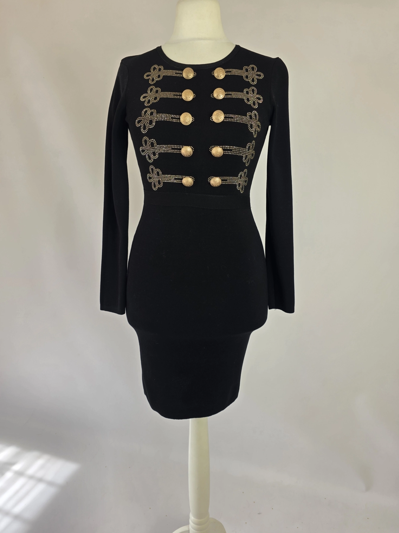 Elegancka czarna sukienka dresowa Allyson Collection ze złotymi guzikami i dżetami doskonale podkreśla kobiecą sylwetkę, łącząc styl militarny z wyjątkową wygodą