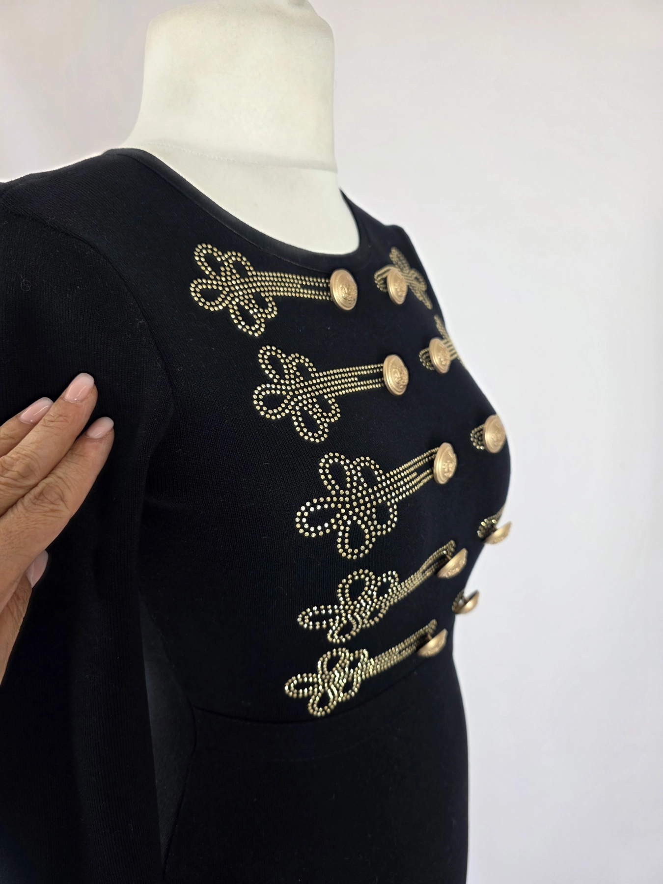 Elegancka czarna sukienka dresowa Allyson Collection ze złotymi guzikami i dżetami doskonale podkreśla kobiecą sylwetkę, łącząc styl militarny z wyjątkową wygodą