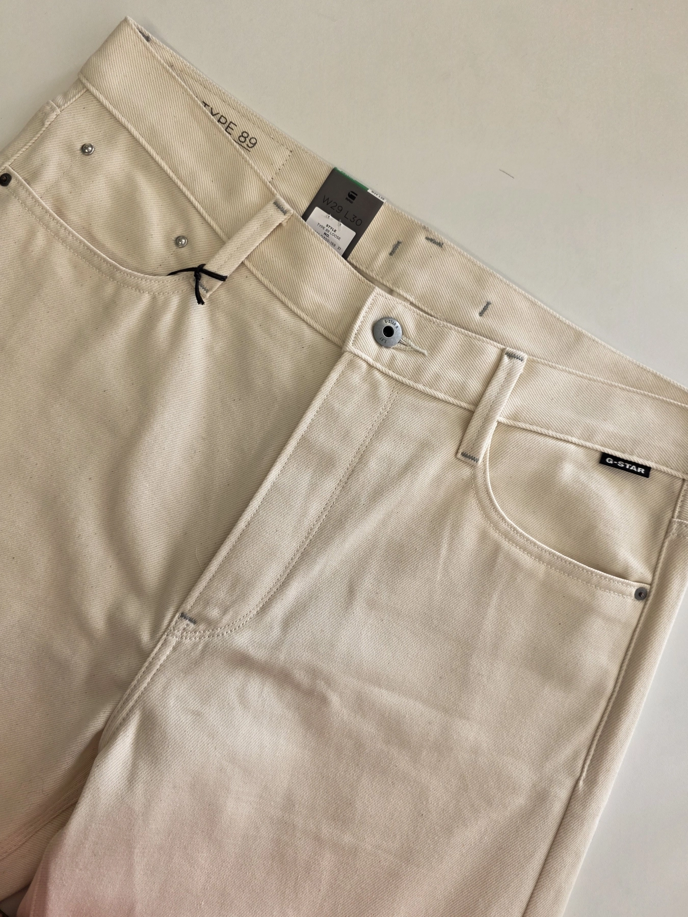 Stylowy komplet damski skomponowany przez stylistkę, składający się z długiego kardiganu Niumi, białej bluzki oraz jasnych spodni G-Star RAW z broszką