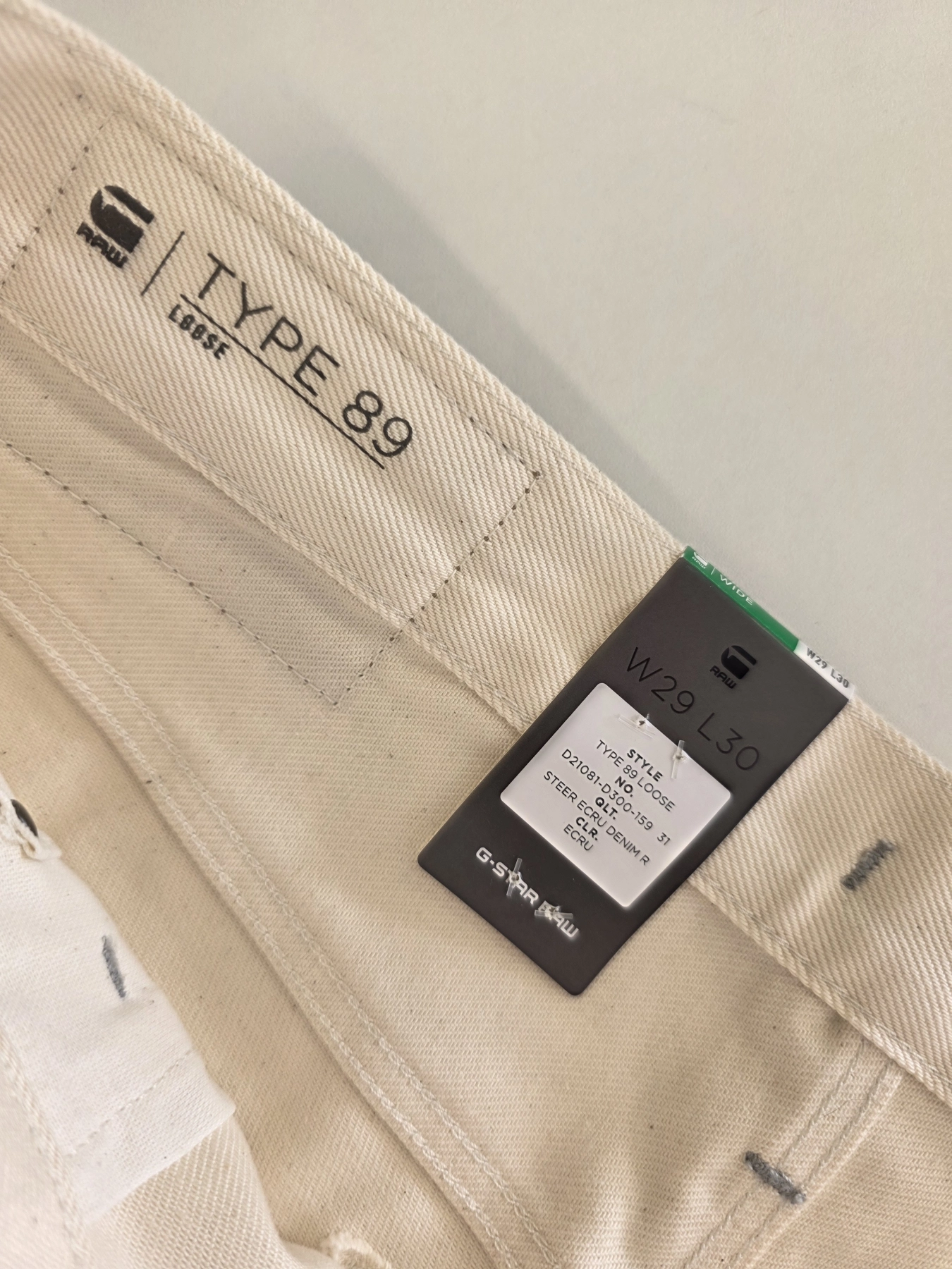 Stylowy komplet damski skomponowany przez stylistkę, składający się z długiego kardiganu Niumi, białej bluzki oraz jasnych spodni G-Star RAW z broszką