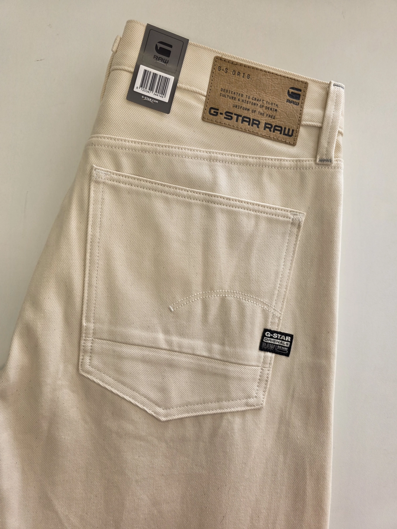 Stylowy komplet damski skomponowany przez stylistkę, składający się z długiego kardiganu Niumi, białej bluzki oraz jasnych spodni G-Star RAW z broszką