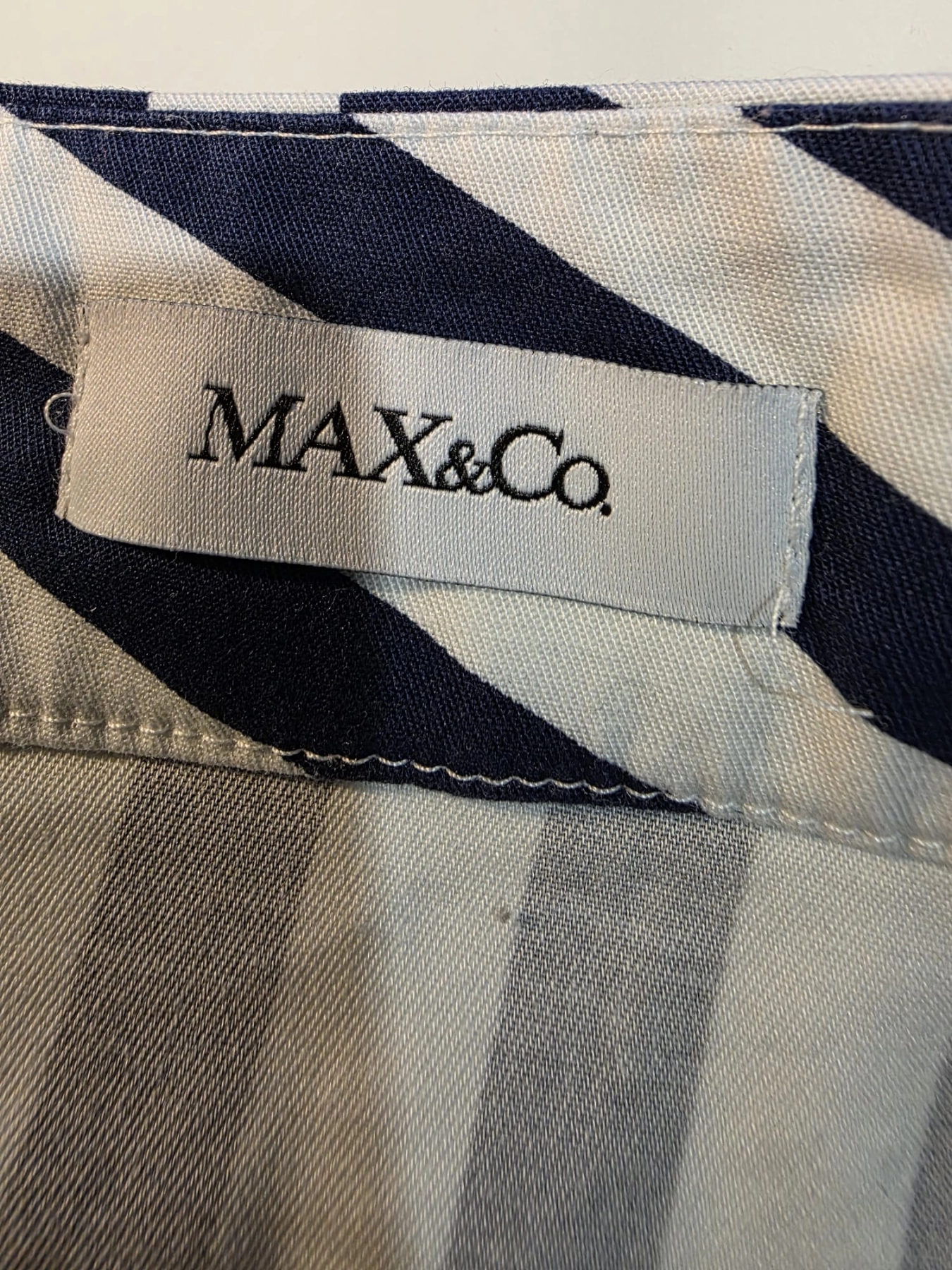 Damski komplet stylizowany przez stylistkę, składający się z zielonej bluzki z długim rękawem oraz kloszowanej spódnicy w geometryczne paski marki MAXandCo. z wygodnymi kieszeniami